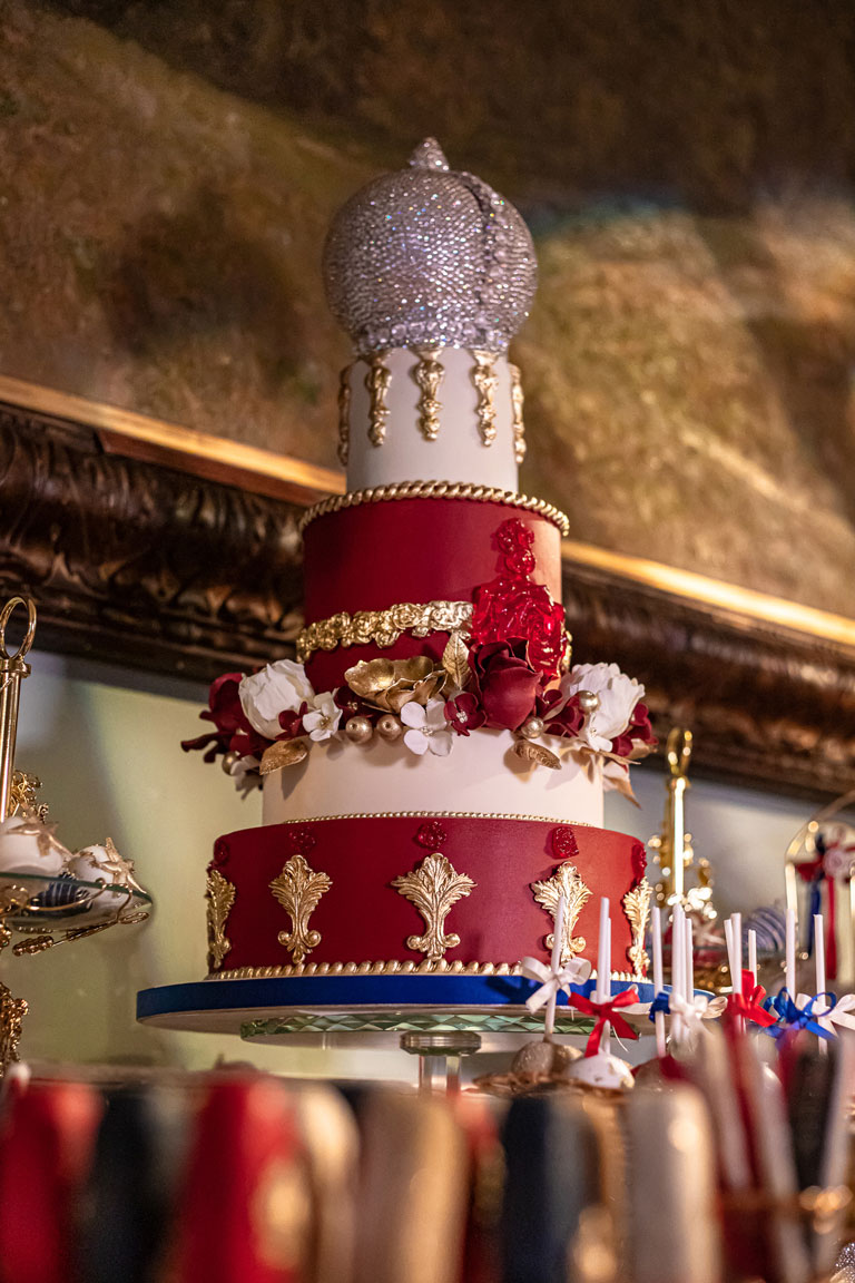 A 4 tiered ornate cake, red, white and gold with a crown of Swarovski crystals on top