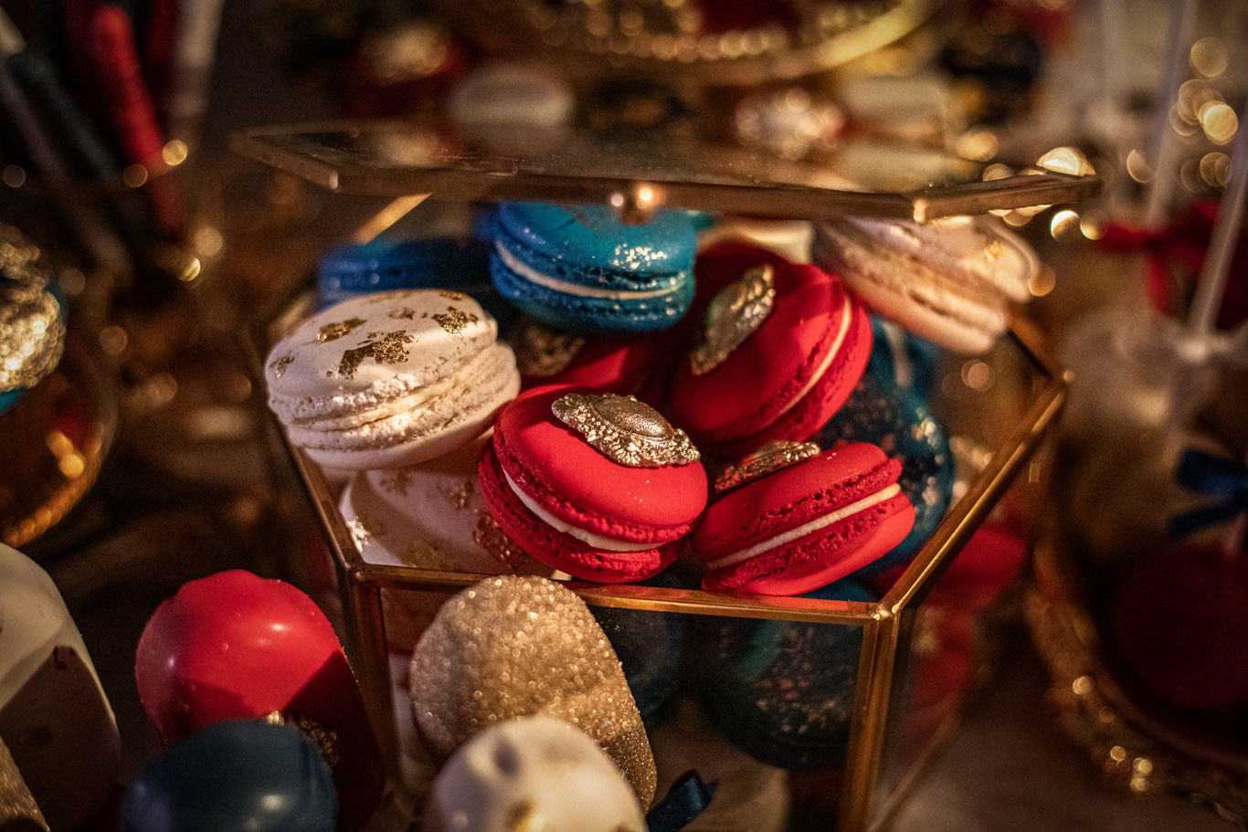 Ornate macarons bursting out of a gold bordered glass box, red, white and blue with elegant designs
