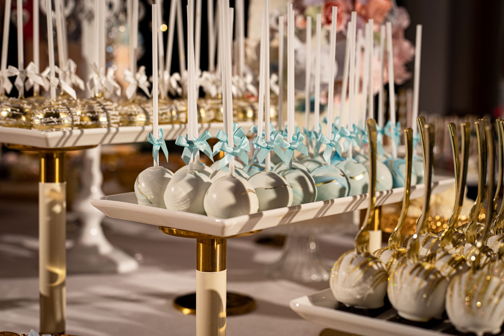 Rows of elegant white and gold cake pops lined up on elegant gold trays