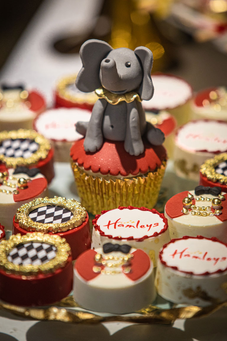 A handmade cake elephant sitting amongst Hamleys branded cupcakes