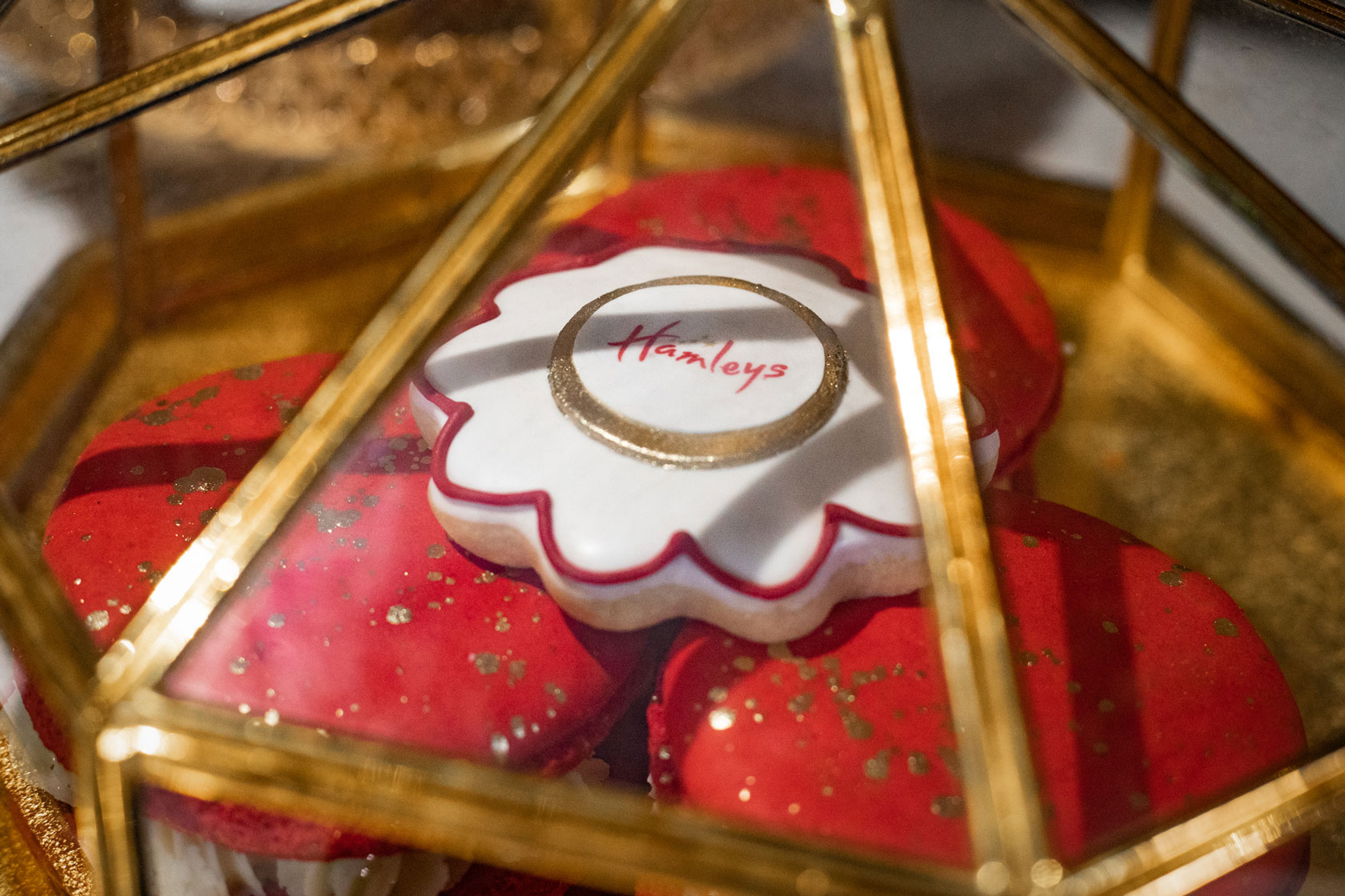 An elegant gold jewelry box with a branded Hamleys cookie and some giant red and gold macarons