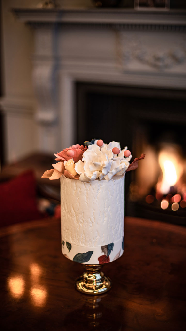 A white bark effect cake topped with hand-crafted sugar flowers in front of the fireplace by GC Couture.